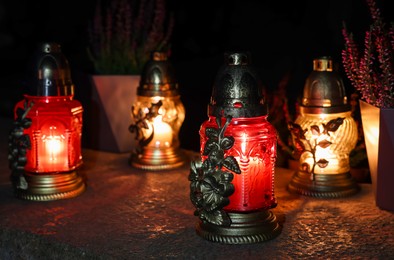 Photo of Different grave lanterns with burning candles on stone surface at night