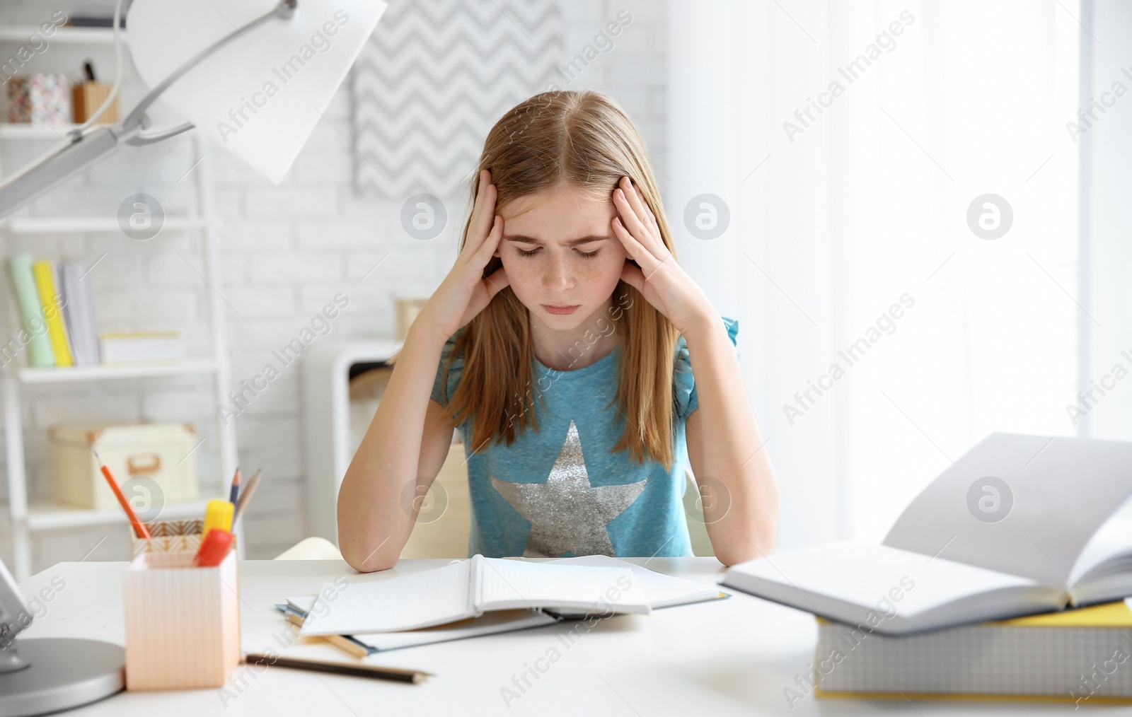 Photo of Teenage girl suffering from headache while doing homework at table indoors