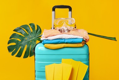 Photo of Suitcase, clothes, beach accessories and tropical leaf on yellow background. Summer vacation