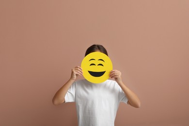 Photo of Little girl covering face with laughing emoji on pale pink background
