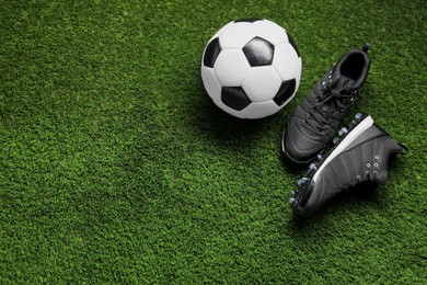Sports equipment. Soccer ball and sneakers on green grass, above view. Space for text