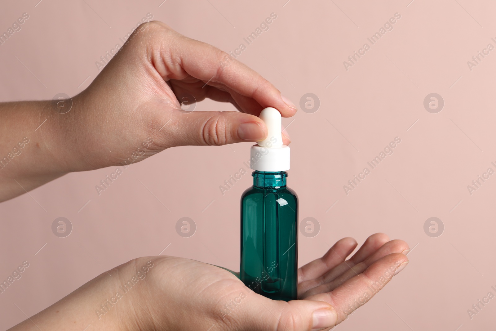 Photo of Woman with bottle of cosmetic serum on light pink background, closeup