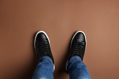 Photo of Man in stylish sneakers standing on brown background, top view