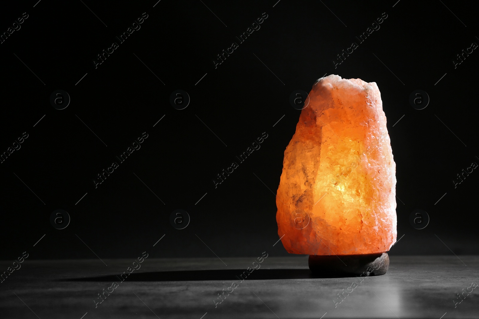 Photo of Himalayan salt lamp on table against black background. Space for text