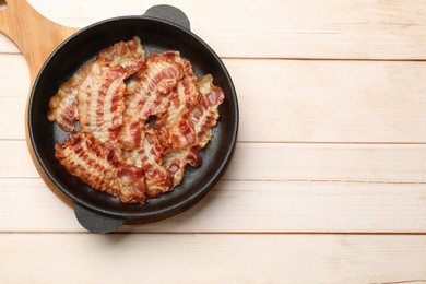 Photo of Delicious bacon slices in frying pan on white wooden table, top view. Space for text