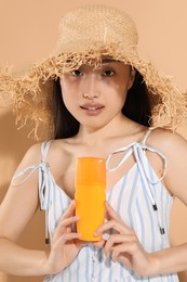 Photo of Beautiful young woman in straw hat holding sun protection cream on beige background