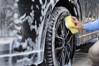 Photo of Businessman cleaning auto with sponge at self-service car wash, closeup