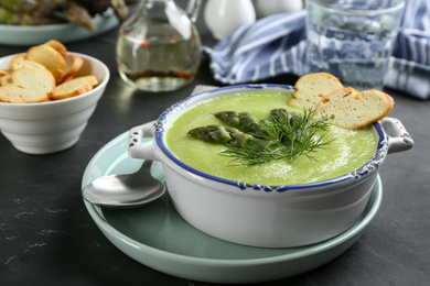 Photo of Delicious asparagus soup served on black table