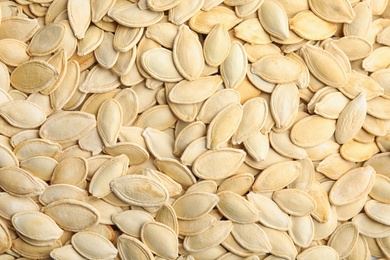 Photo of Raw unpeeled pumpkin seeds as background, top view