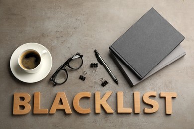 Photo of Word Blacklist of wooden letters, cup with coffee and office stationery on grey table, flat lay