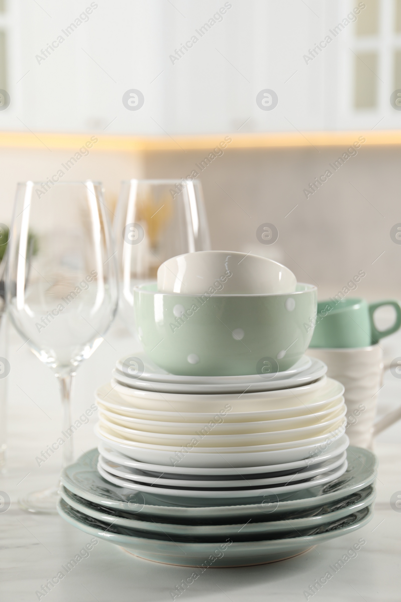 Photo of Many different clean dishware and glasses on white marble table in kitchen