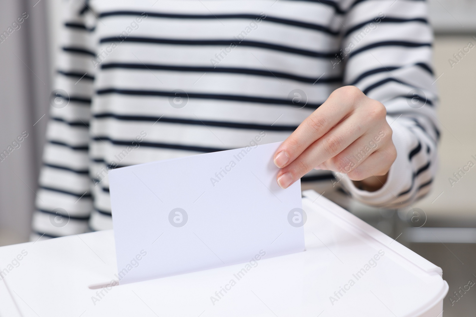 Photo of Woman putting her vote into ballot box on blurred background, closeup