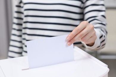 Photo of Woman putting her vote into ballot box on blurred background, closeup