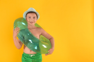 Cute little child in beachwear with bright inflatable ring on yellow background. Space for text