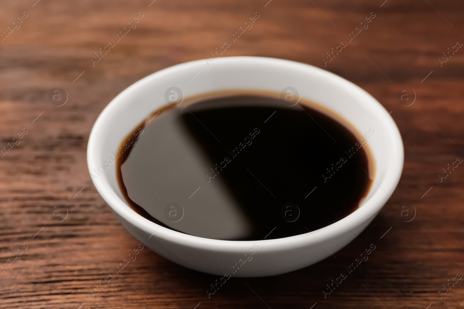 Photo of Bowl with soy sauce on wooden table, closeup