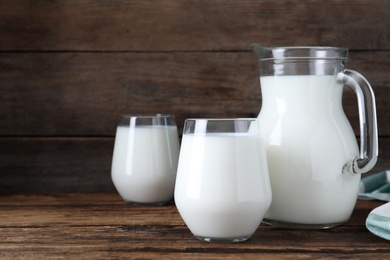 Photo of Jug and glasses with fresh milk on wooden table. Space for text