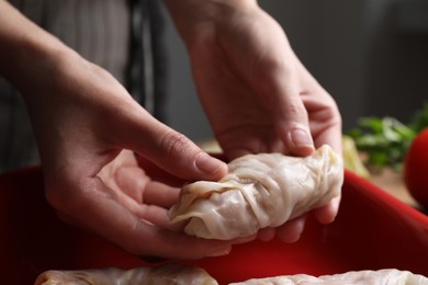 Woman putting uncooked stuffed cabbage roll into baking dish at table, closeup