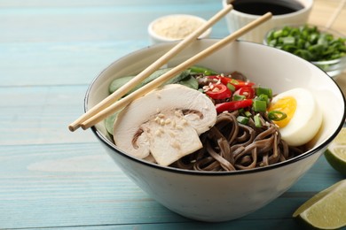 Photo of Tasty buckwheat noodles (soba) with chili pepper, egg, mushrooms and chopsticks on light blue wooden table, closeup