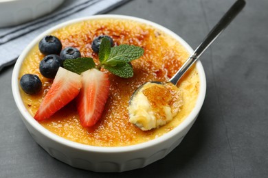 Photo of Delicious creme brulee with berries in bowl and spoon on grey table, closeup