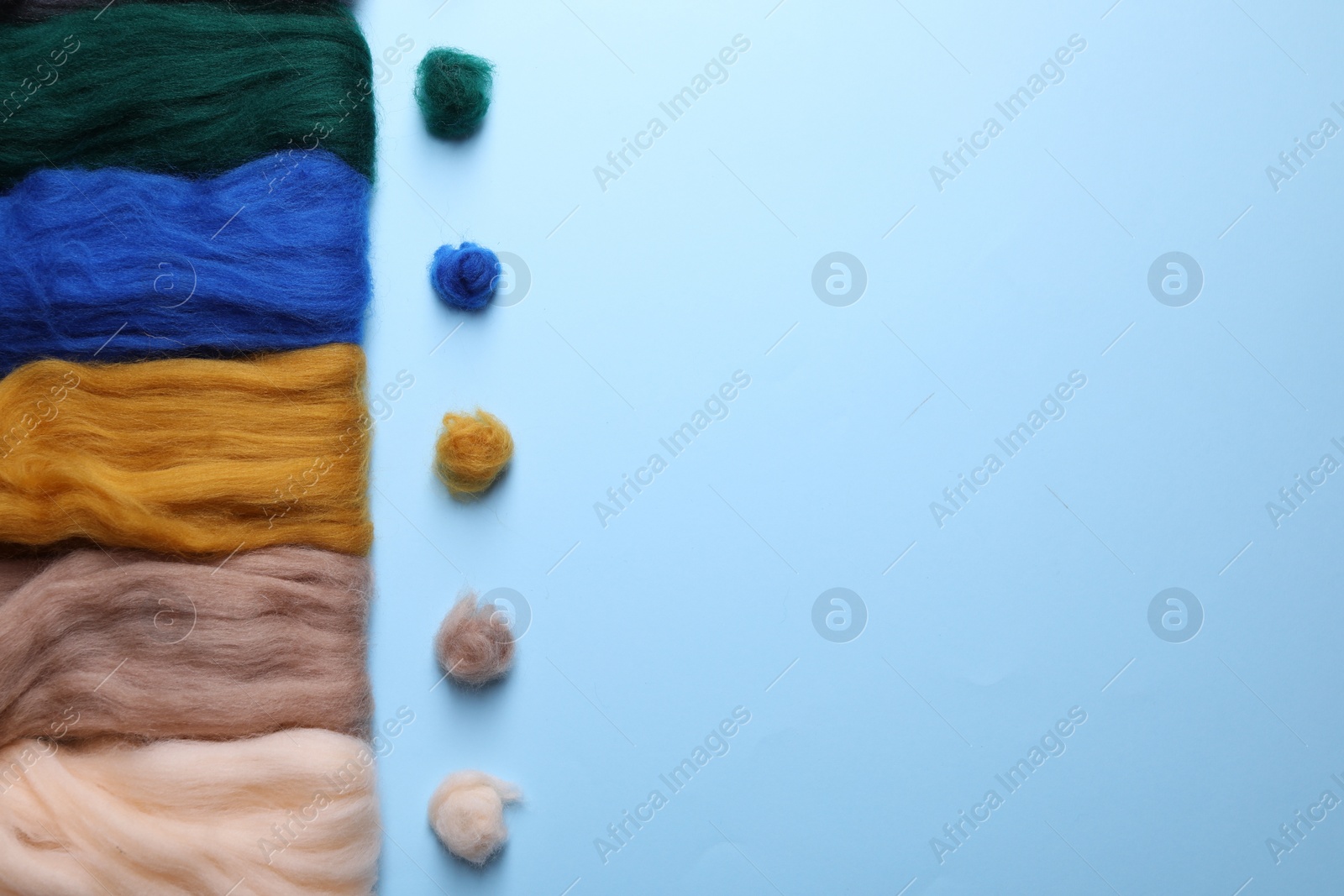 Photo of Colorful felting wool and balls on light blue background, flat lay. Space for text