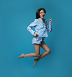 Photo of Beautiful Asian woman in pajamas jumping on blue background. Bedtime
