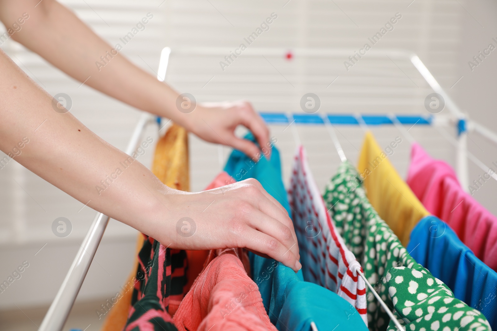 Photo of Woman hanging clean laundry on drying rack indoors, closeup