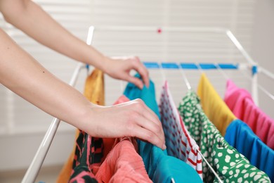 Photo of Woman hanging clean laundry on drying rack indoors, closeup