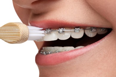 Woman with dental braces cleaning teeth on white background, closeup