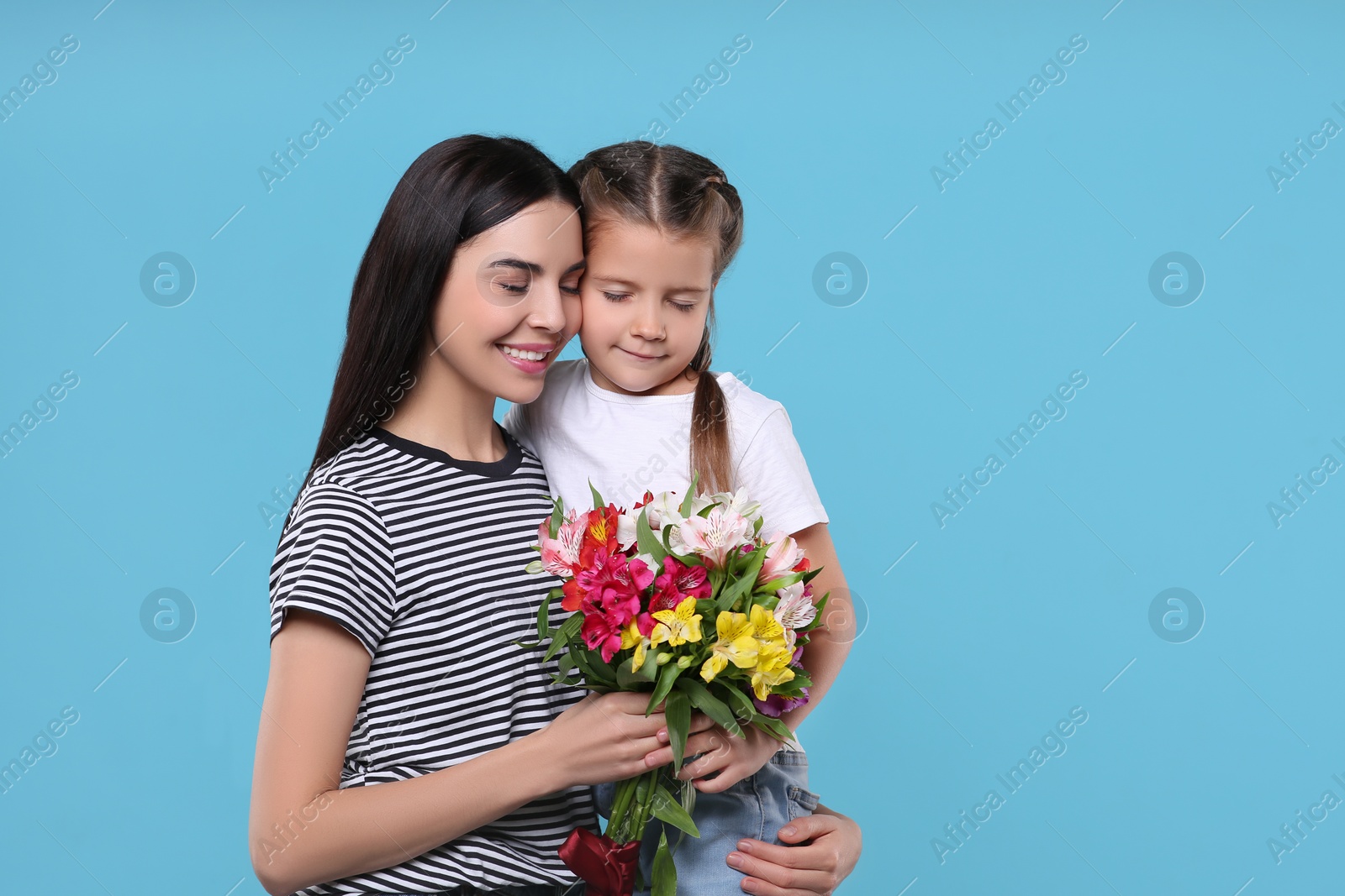 Photo of Happy woman with her daughter and bouquet of beautiful flowers on light blue background, space for text. Mother's day celebration