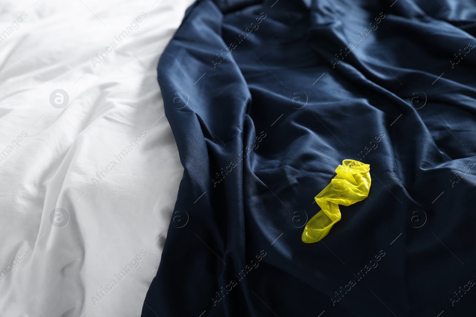 Photo of Unrolled condom on bed in bedroom. Safe sex