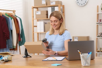 Photo of Seller with scanner reading parcel barcode at table in office. Online store