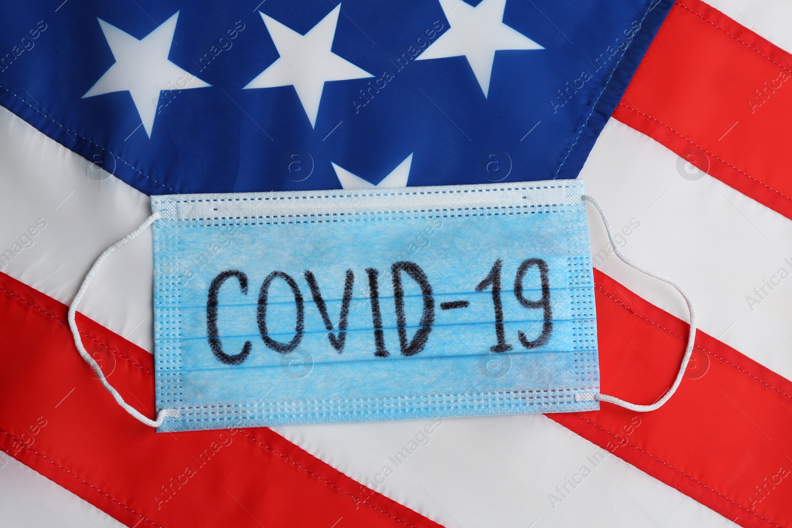 Photo of Medical mask with word COVID-19 on American flag, top view. Coronavirus pandemic in USA