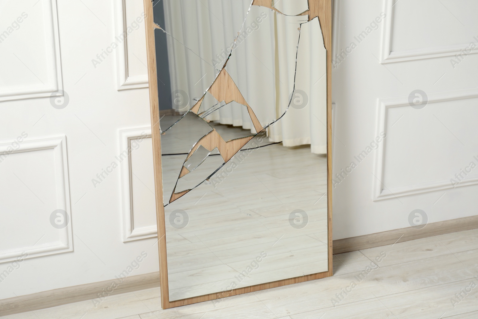 Photo of Broken mirror with many cracks near white wall indoors