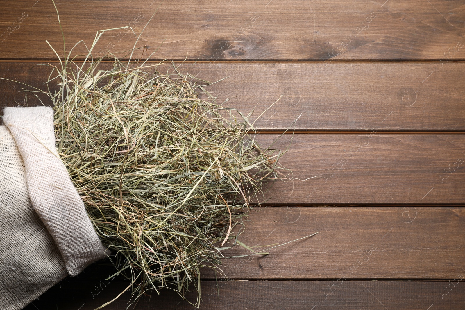 Photo of Dried hay in burlap sack on wooden table, top view. Space for text