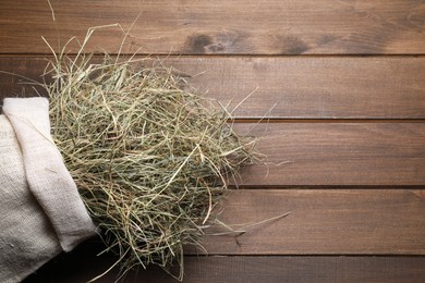Photo of Dried hay in burlap sack on wooden table, top view. Space for text