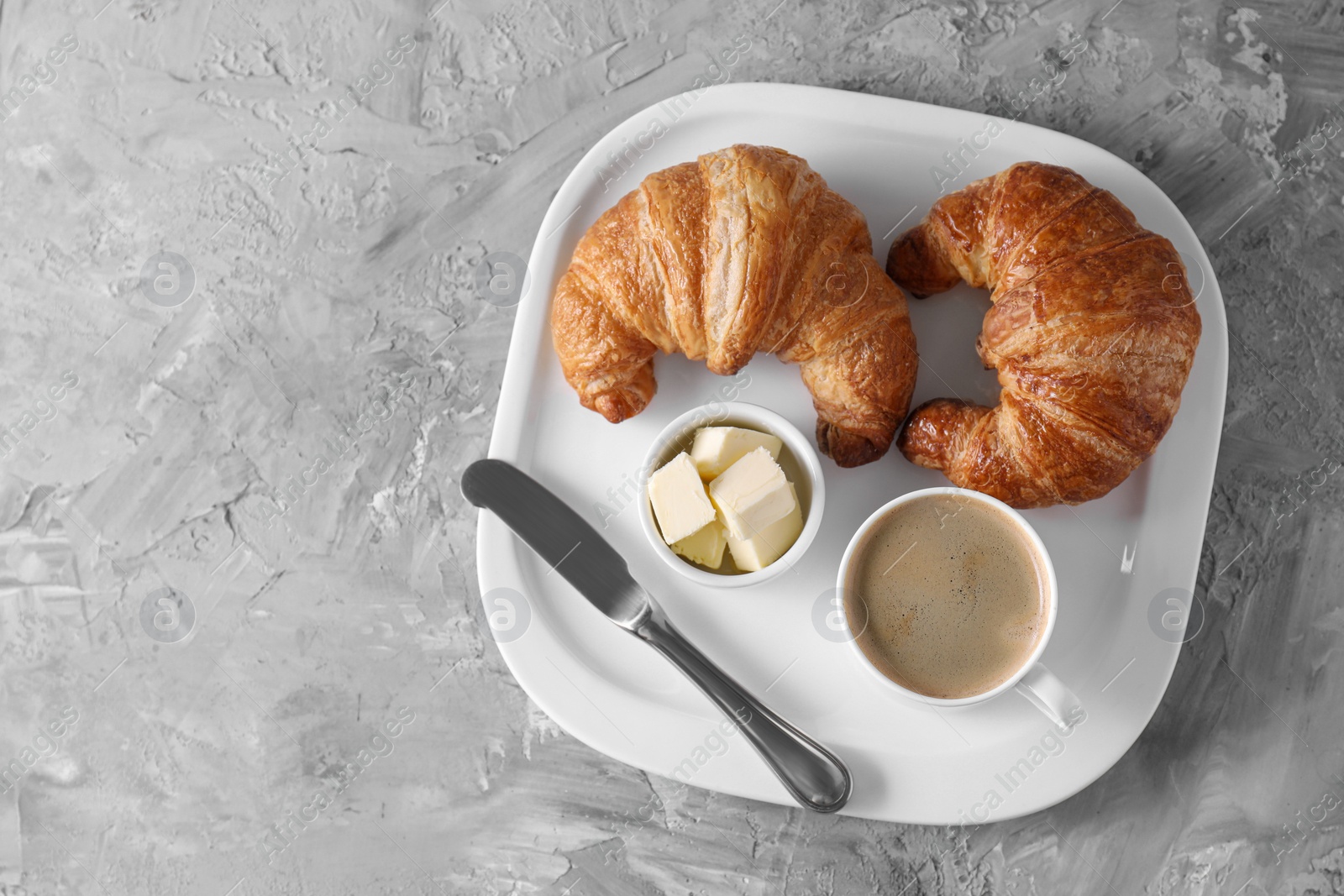 Photo of Tasty breakfast. Cup of coffee, fresh croissants, knife and butter on grey table, top view. Space for text