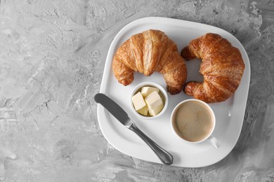 Tasty breakfast. Cup of coffee, fresh croissants, knife and butter on grey table, top view. Space for text