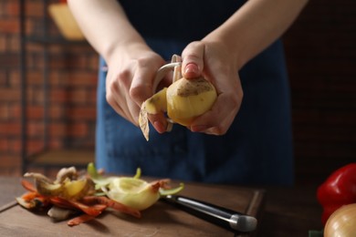 Photo of Woman peeling fresh potato at table indoors, closeup