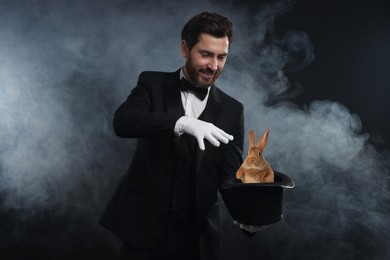 Image of Magician showing trick with top hat and rabbit in smoke on dark background
