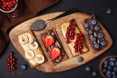 Fresh crunchy rye crispbreads with different toppings on black table, flat lay