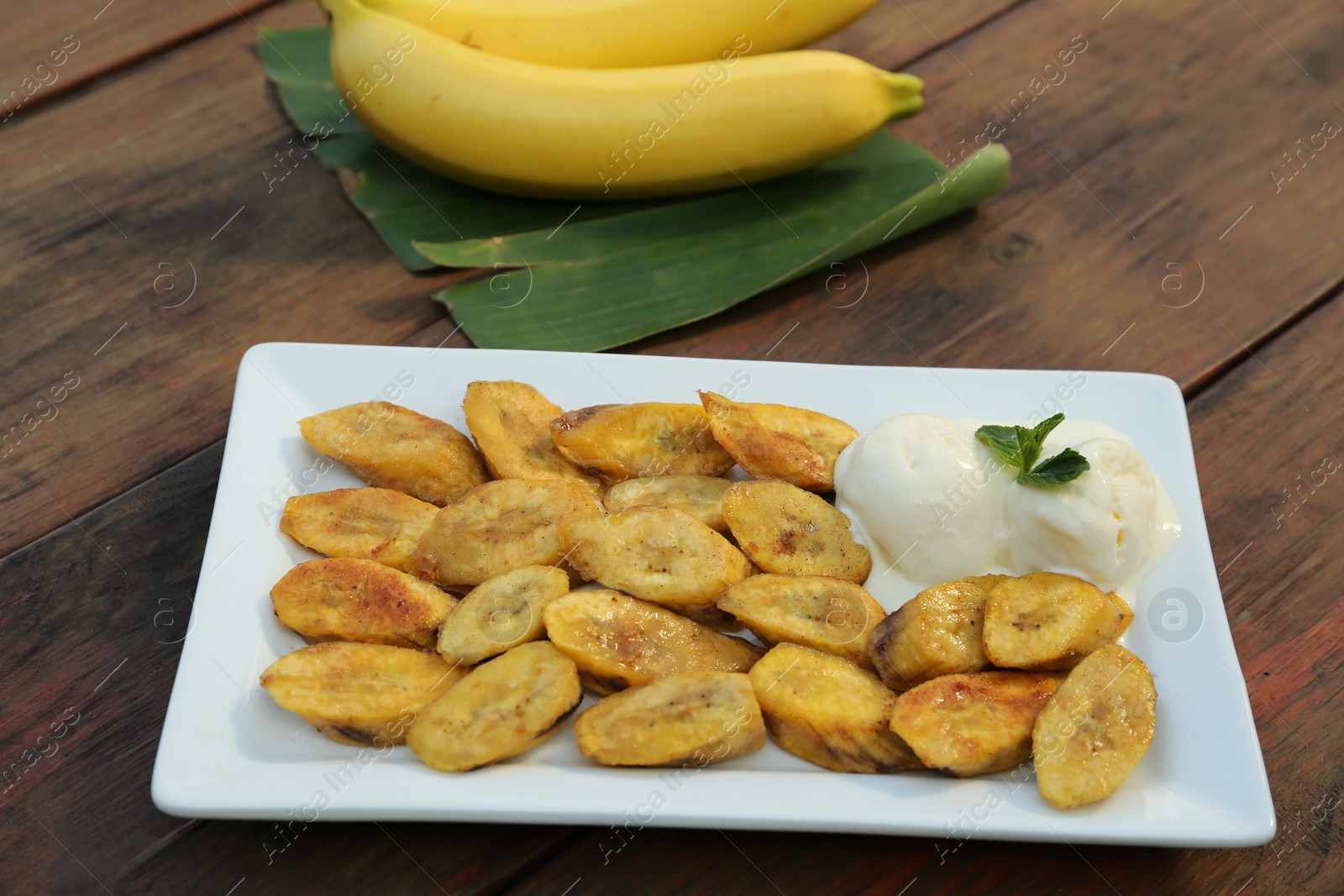 Photo of Tasty deep fried banana slices with ice cream and mint on wooden table