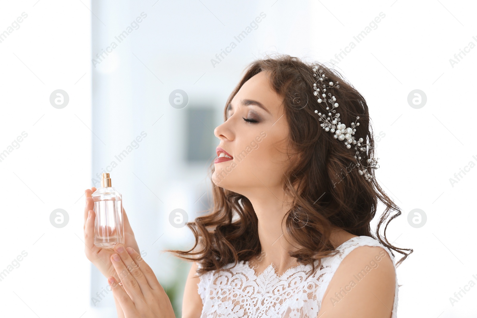 Photo of Beautiful young bride with bottle of perfume on blurred background