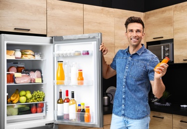 Photo of Man with bottle of juice near refrigerator in kitchen