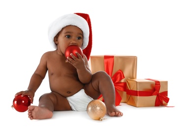 Photo of Cute African-American baby wearing Santa hat with Christmas gifts on white background