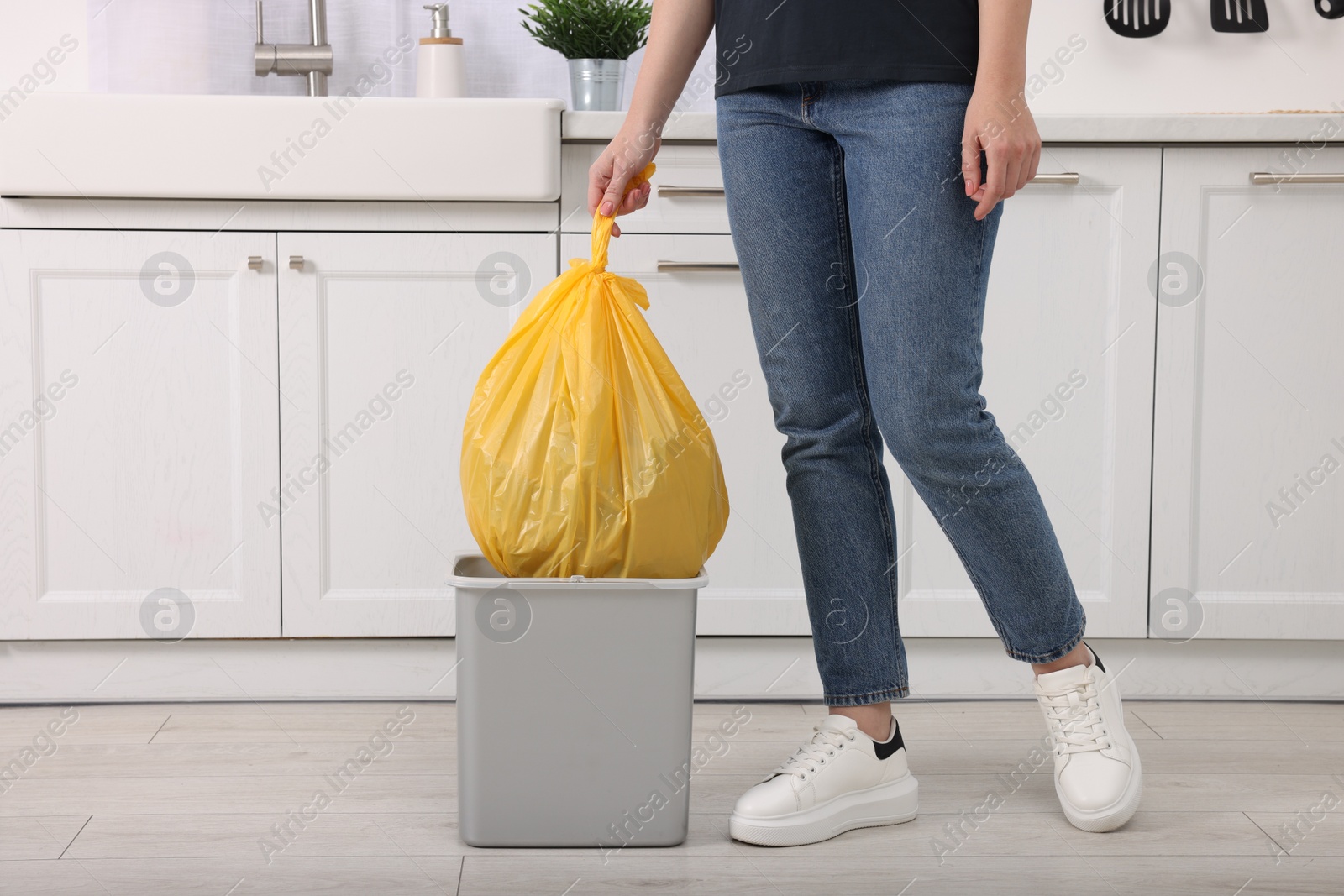 Photo of Woman taking garbage bag out of trash bin in kitchen, closeup