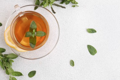 Photo of Glass cup of delicious immunity boosting tea with lemon and mint on light grey table, flat lay. Space for text