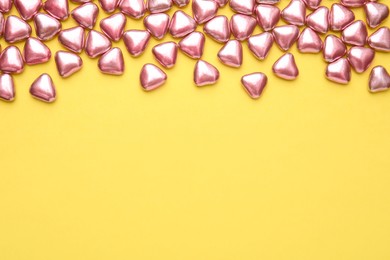 Photo of Many delicious heart shaped candies on yellow background, flat lay. Space for text