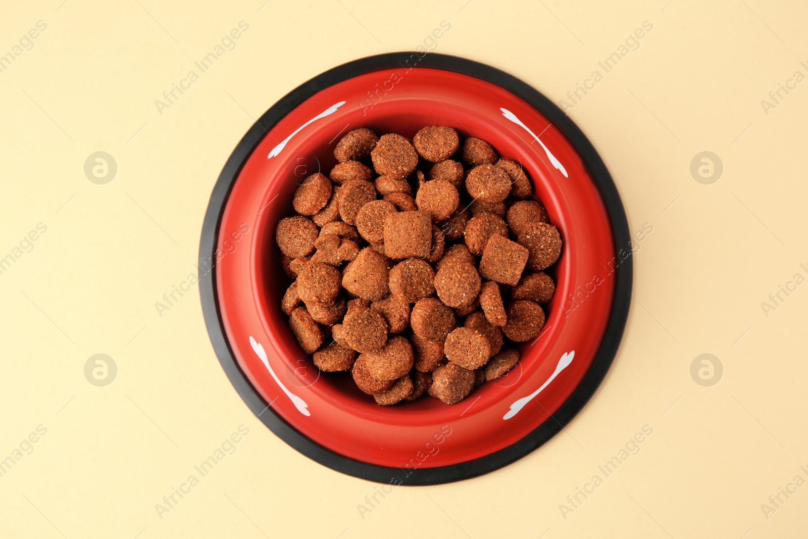 Photo of Dry dog food in feeding bowl on beige background, top view