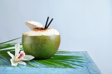 Fresh green coconut with drinking straws and flower on table against light background