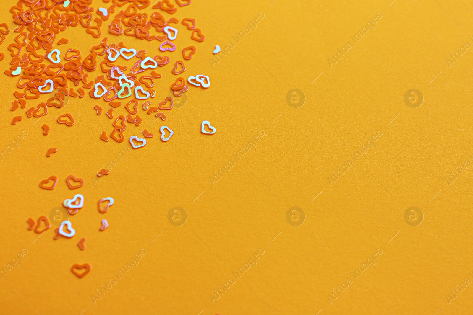 Photo of Shiny bright heart shaped glitter on pale orange background. Space for text